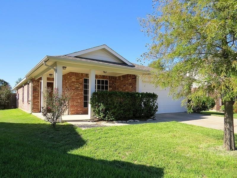 This is a single-story brick house featuring a two-car garage, a well-maintained lawn, and mature landscaping. The home offers a welcoming entrance with a covered front porch.