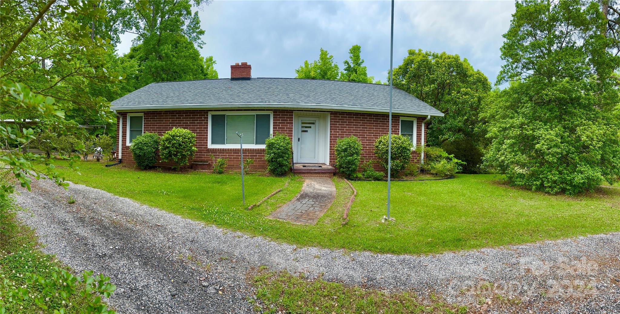 a view of a brick house with a yard plants and large tree