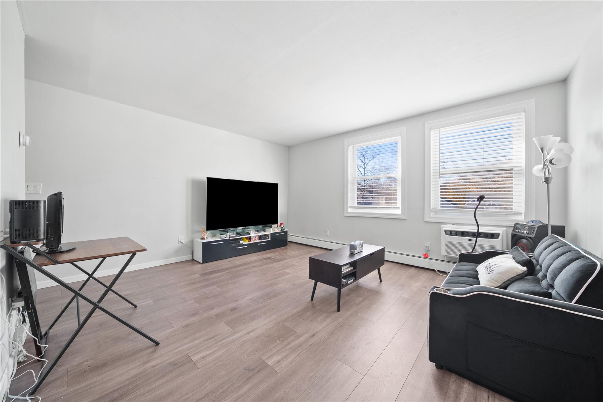 Living room with a baseboard radiator, a wall mounted air conditioner, and light wood-type flooring