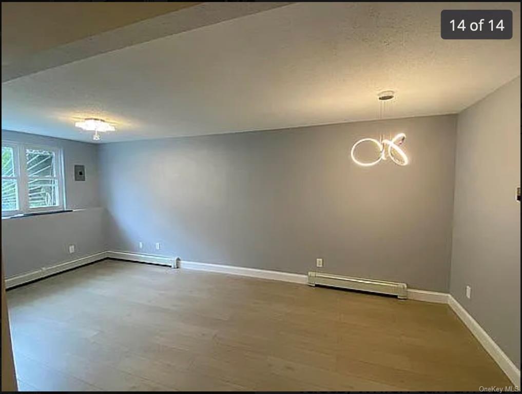 Unfurnished room featuring light hardwood / wood-style floors, a notable chandelier, and a baseboard radiator