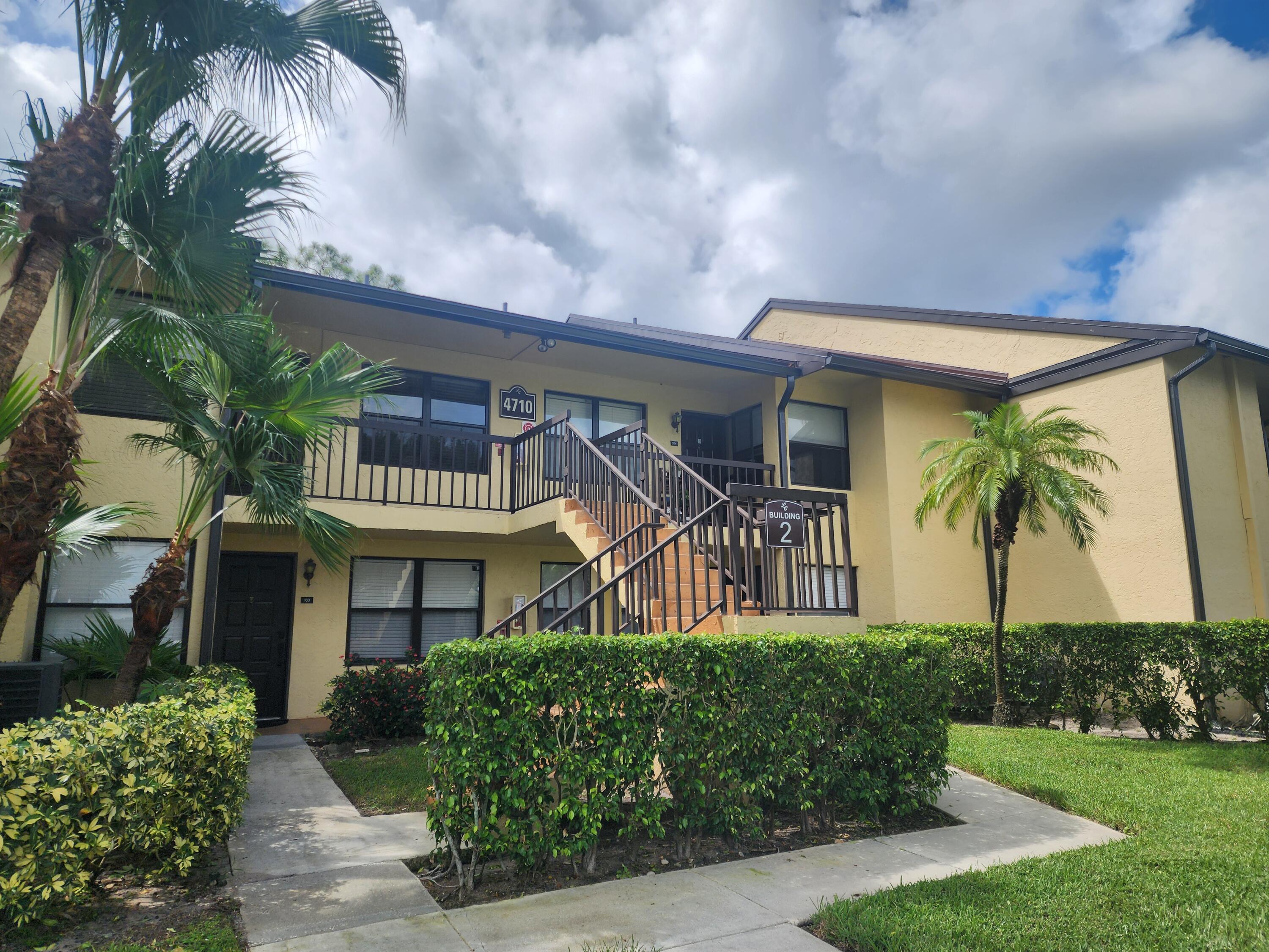 a front view of multi story residential apartment building with yard and bench and trees