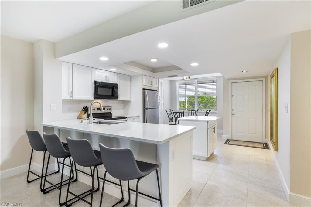 Kitchen featuring light tile patterned flooring, kitchen peninsula, white cabinetry, appliances with stainless steel finishes, and a kitchen bar