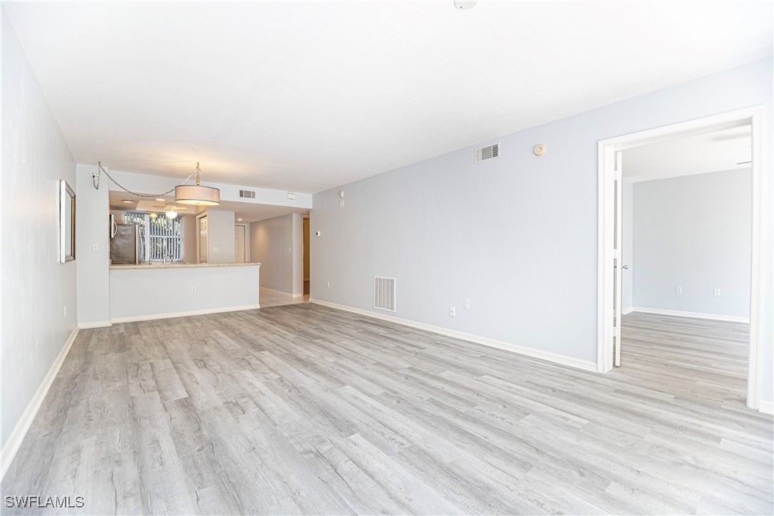 a view of empty room with wooden floor and kitchen view