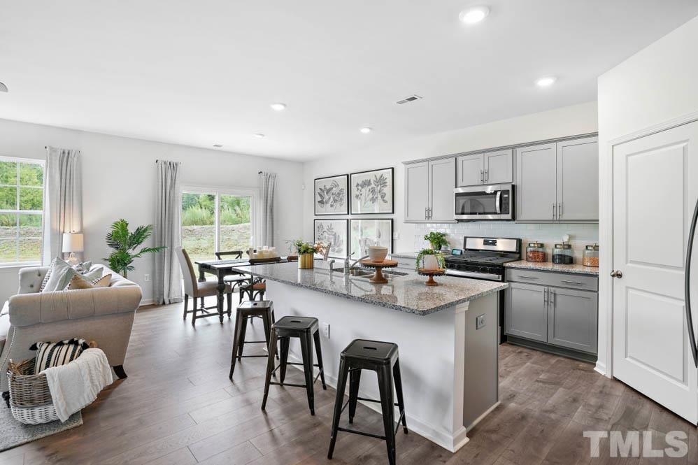 a kitchen with stainless steel appliances kitchen island granite countertop a table chairs microwave and cabinets