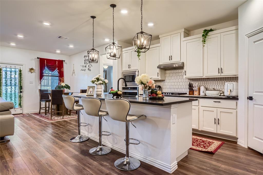 a room with stainless steel appliances kitchen island granite countertop a table chairs in it and wooden floors