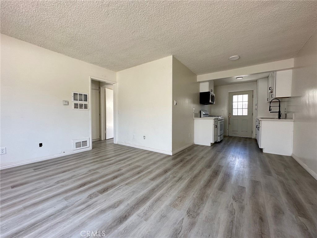 a view of empty room with wooden floor and kitchen