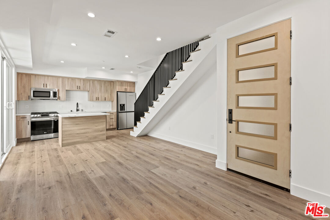 an empty room with wooden floors and kitchen view