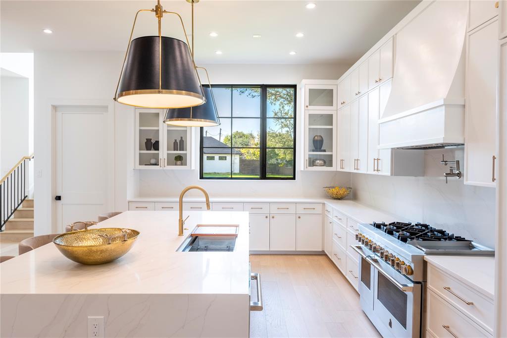 Kitchen with custom exhaust hood, white cabinetry, sink, range with two ovens, and decorative light fixtures