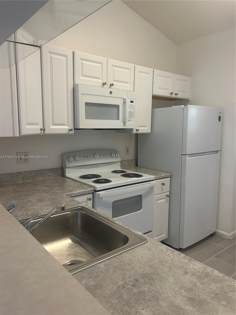 a kitchen with refrigerator a stove a white cabinet and a granite counter tops