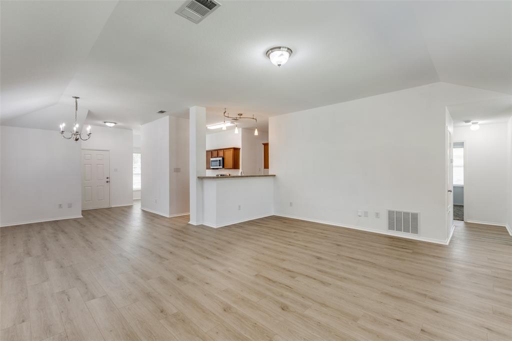 an empty room with wooden floor and kitchen view