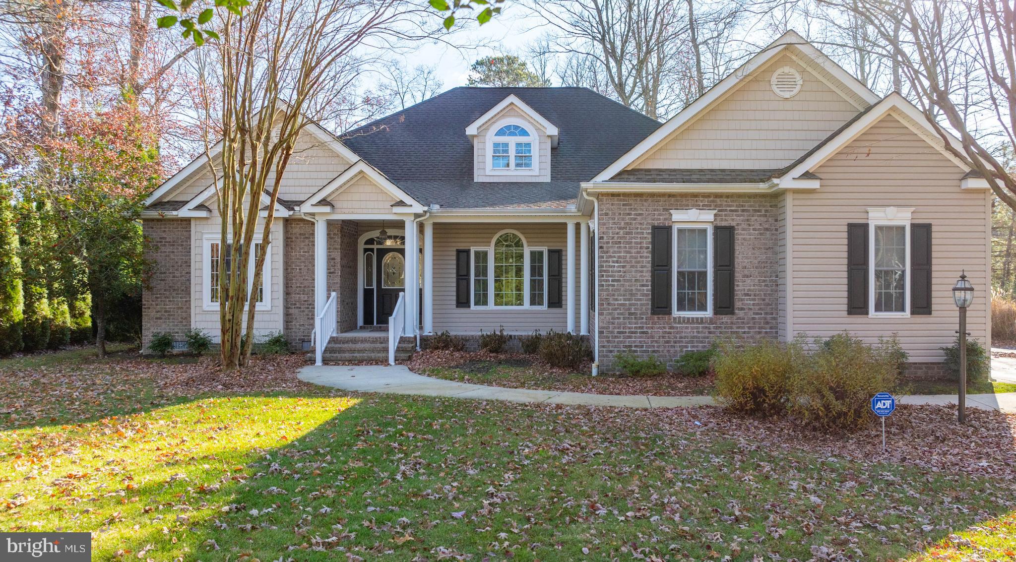 a view of a brick house with a yard plants and large tree