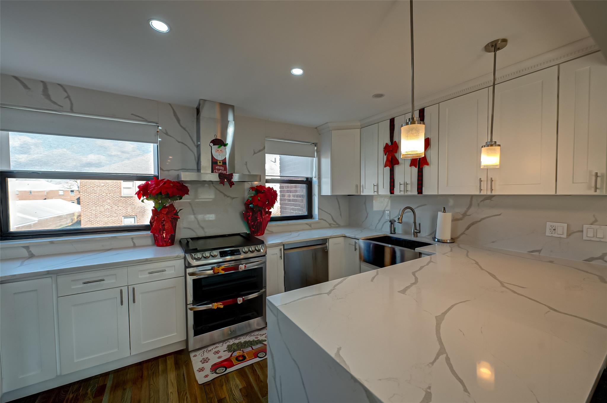 Kitchen featuring light stone counters, stainless steel appliances, sink, pendant lighting, and range hood