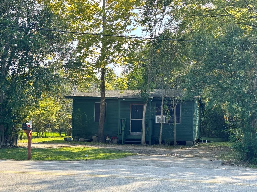 a view of a house in front of a yard with plants and large trees