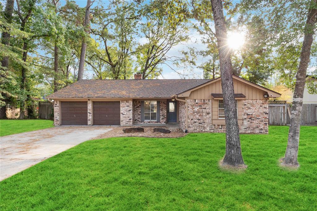 Charming single-story home with a spacious two-car garage, featuring a mix of brick and wood siding exterior, nestled among mature trees with a well-maintained lawn.