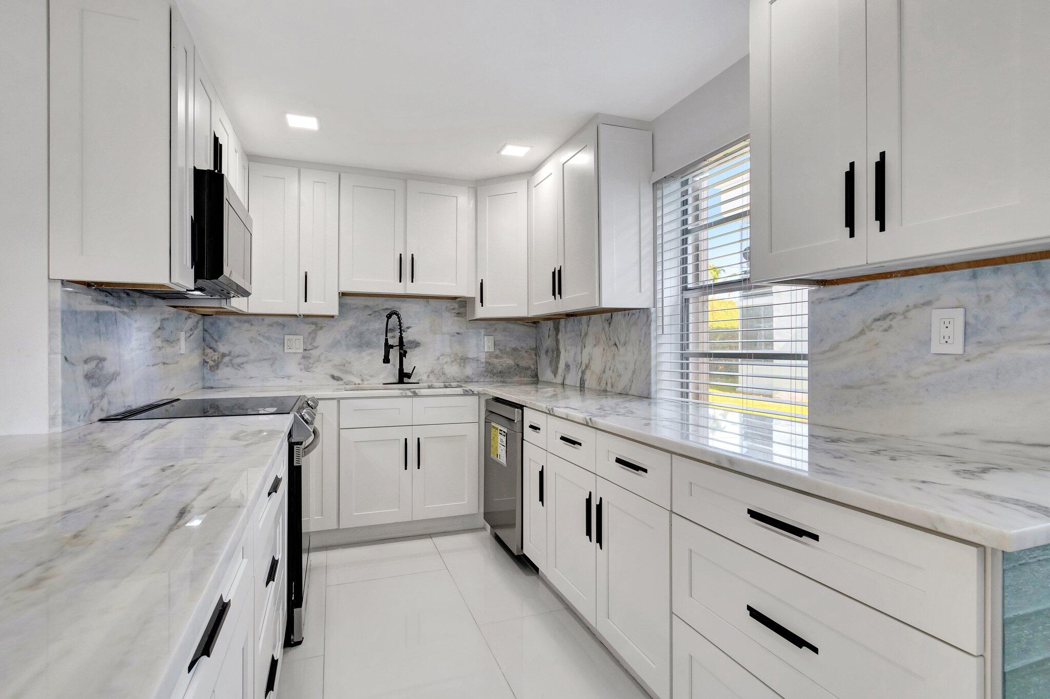 a kitchen with granite countertop white cabinets white stainless steel appliances a sink and a window