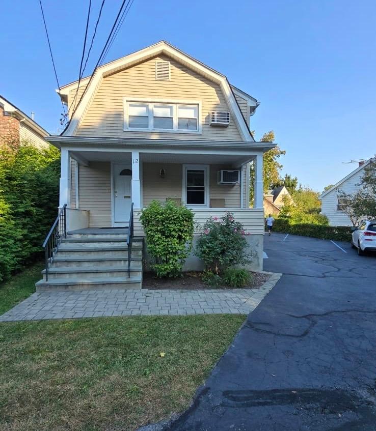 Bungalow-style home featuring a front yard, a porch, and a wall mounted AC