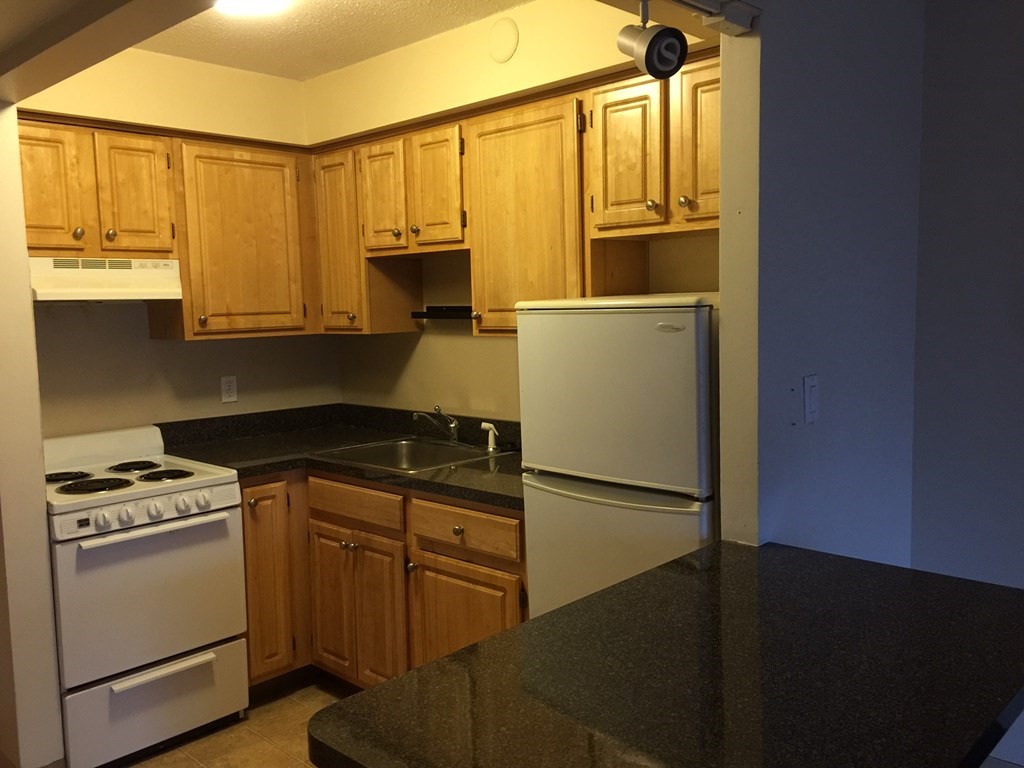 a kitchen with granite countertop a refrigerator a sink and white cabinets