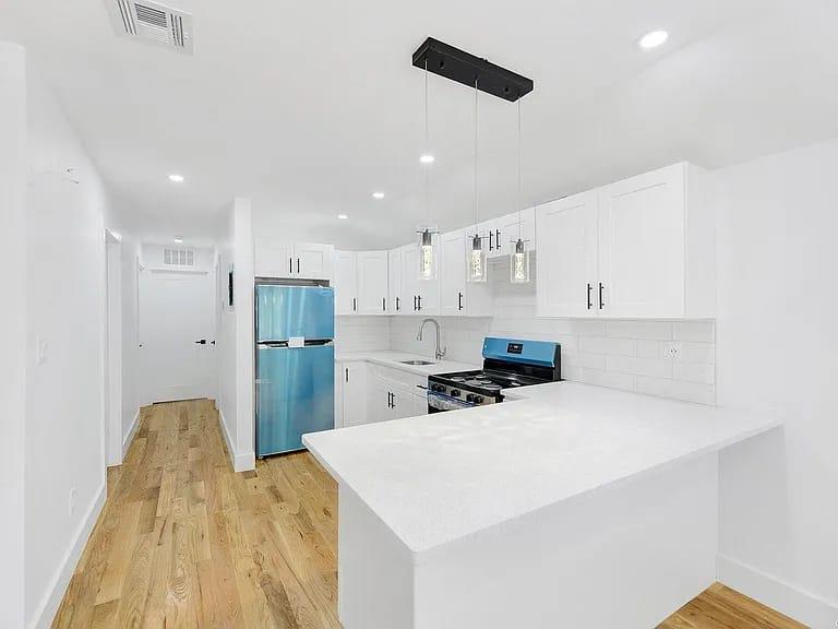 Kitchen with decorative backsplash, stainless steel fridge, black gas stove, white cabinetry, and hanging light fixtures