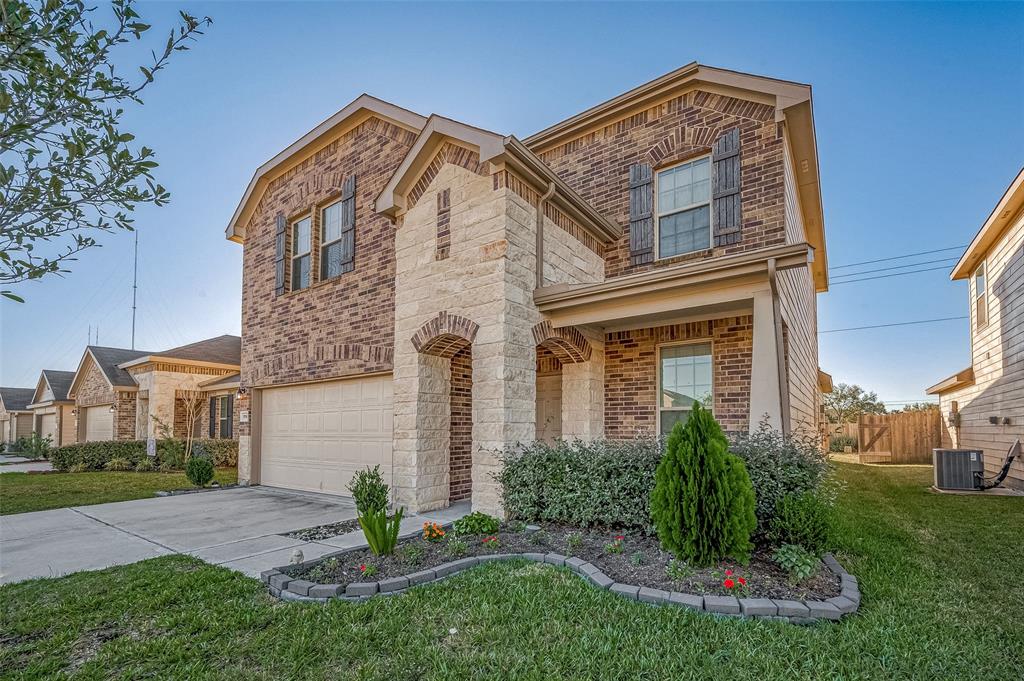 This is a two-story brick home featuring an attached two-car garage, arched entryway, and landscaped front yard.