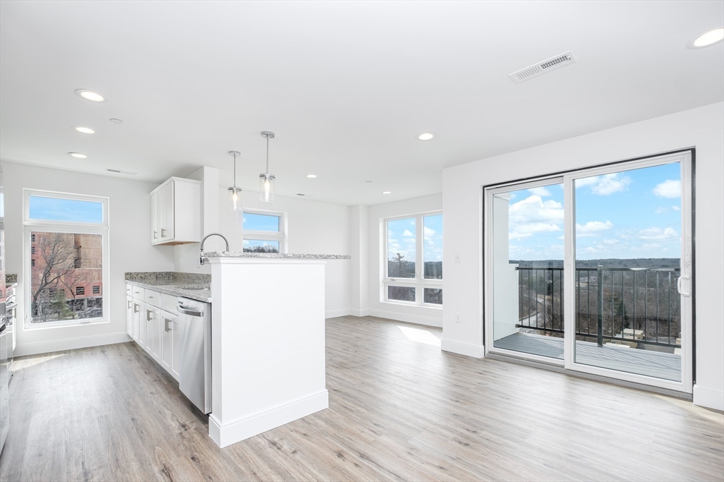 a kitchen with stainless steel appliances granite countertop a stove a refrigerator a sink and white cabinets with wooden floor next to windows