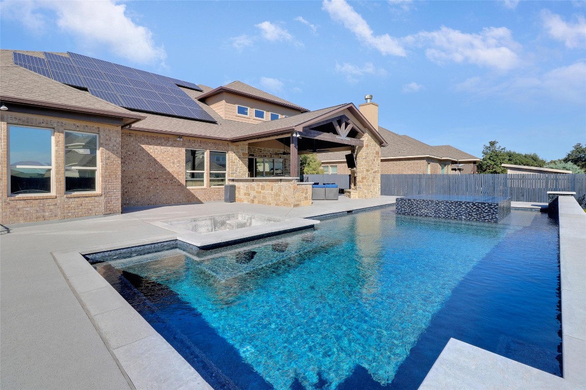 Beyond the outdoor living area, a show-stopping pool area awaits, complete with a hot tub, a waterfall feature, and a distinctive sunken seating area that extends seamlessly from the pool.