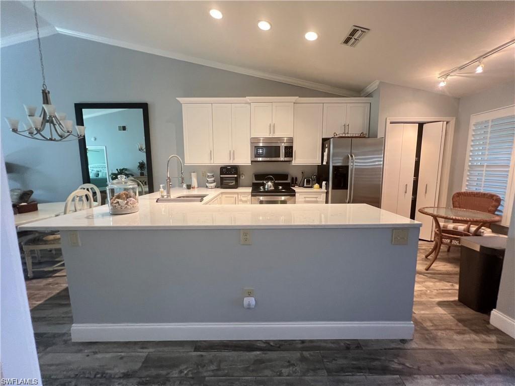 Kitchen with vaulted ceiling, white cabinetry, stainless steel appliances, an inviting chandelier, and sink