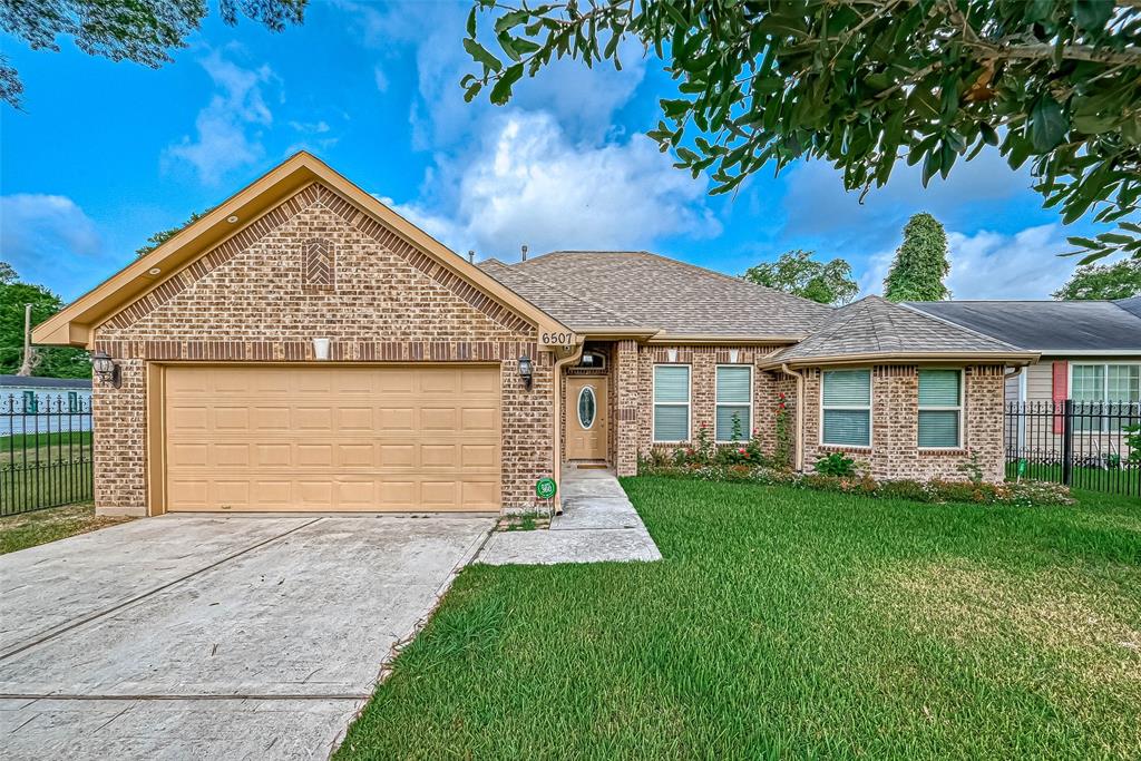 This is a single-story brick home featuring a two-car garage, a well-manicured lawn, and a welcoming entrance with a decorative front door.