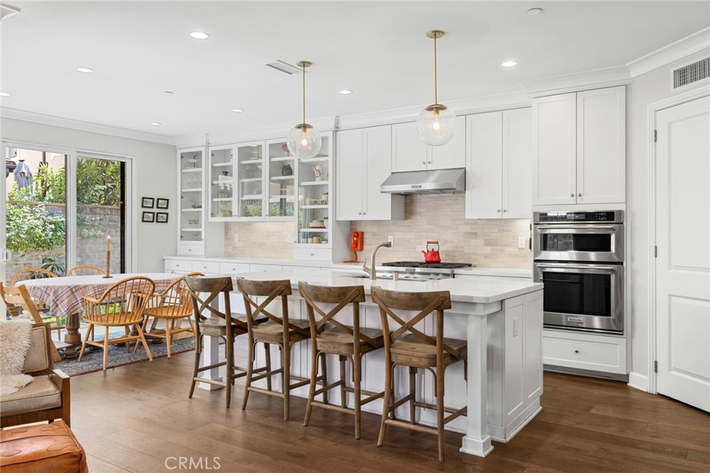 Upgraded quartz countertops and white Shaker cabinetry with glass uppers enhance the kitchen’s upscale aesthetic, and a walk-in pantry, stone-tile backsplash, and a full suite of stainless steel KitchenAid and Bosch appliances is featured.