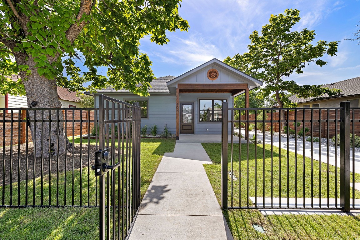 a view of a brick house in front of a yard with plants and large trees