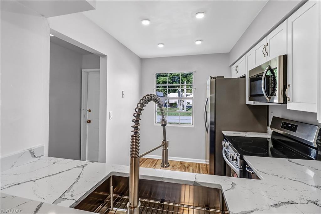 Kitchen with white cabinetry, light wood-type flooring, sink, light stone countertops, and appliances with stainless steel finishes