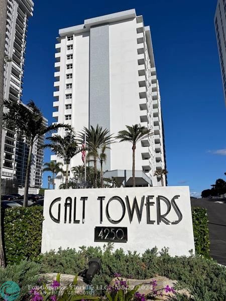 a sign broad with a building and trees in the background