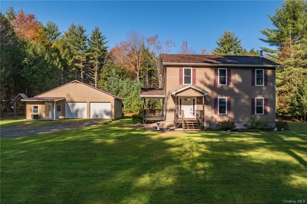 Colonial inspired home featuring a garage, a front lawn, and an outbuilding