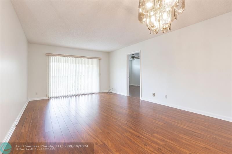 an empty room with wooden floor chandelier fan and windows