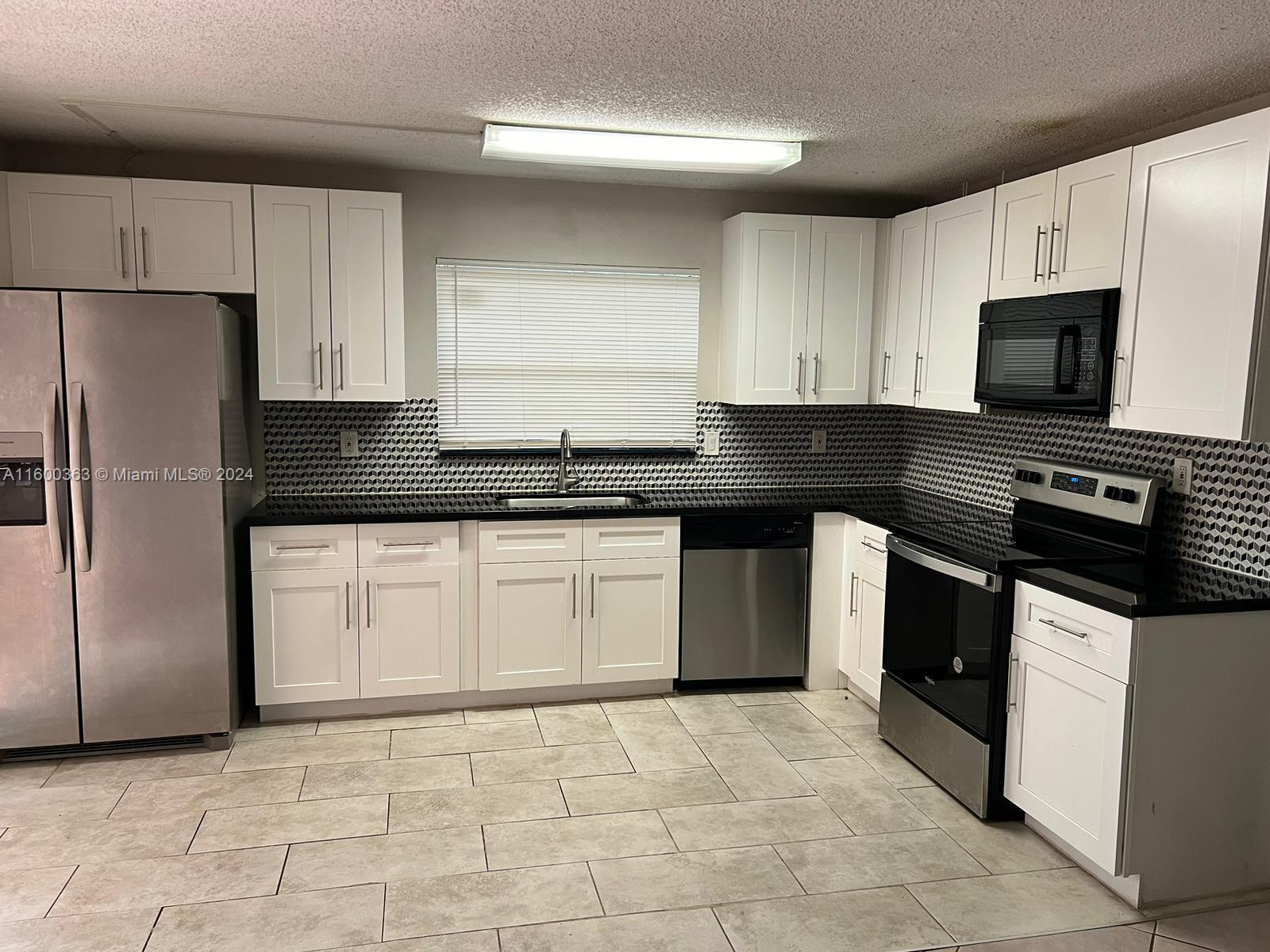 a kitchen with granite countertop a refrigerator sink and white cabinets