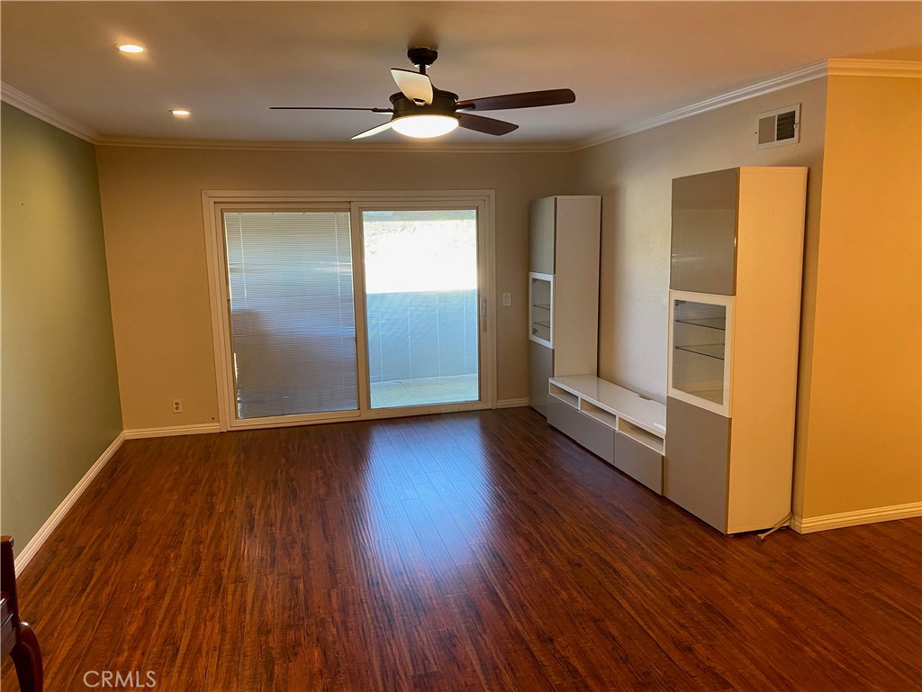 a view of an empty room with wooden floor and a ceiling fan