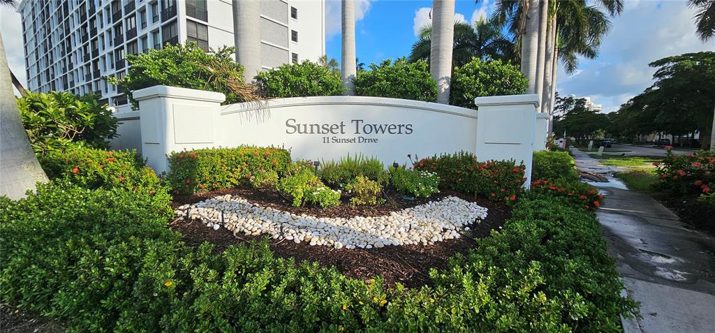 a view of a sign in a garden with a building in the background