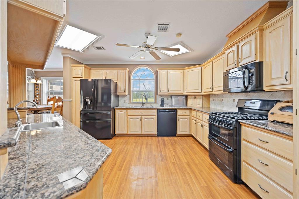 a large kitchen with stainless steel appliances granite countertop a large stove a sink dishwasher and white cabinets with wooden floor