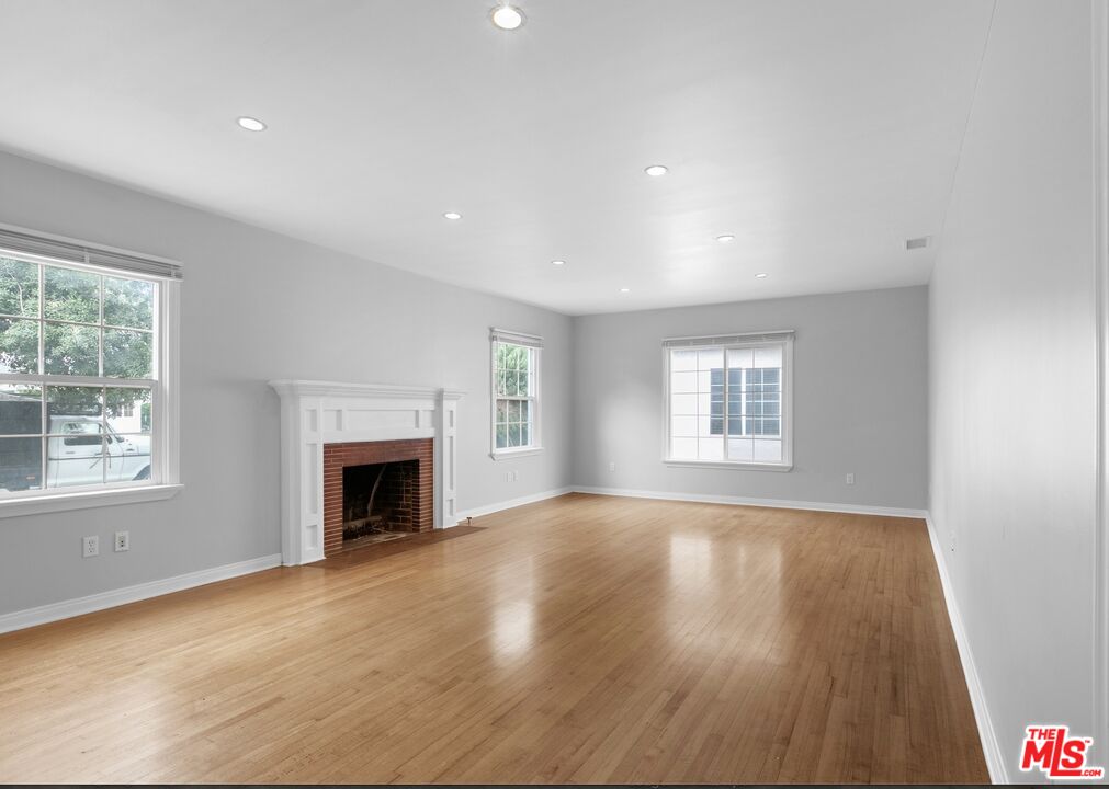 an empty room with wooden floor fireplace and windows