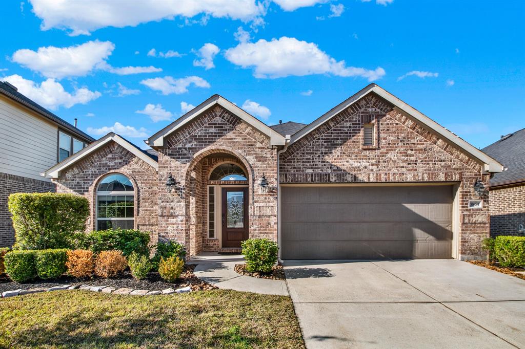 This charming home features a classic brick exterior with arched windows and a welcoming entryway. It includes a two-car garage and a neatly landscaped front yard, set against a bright blue sky. Perfect for those seeking a cozy and attractive suburban residence.