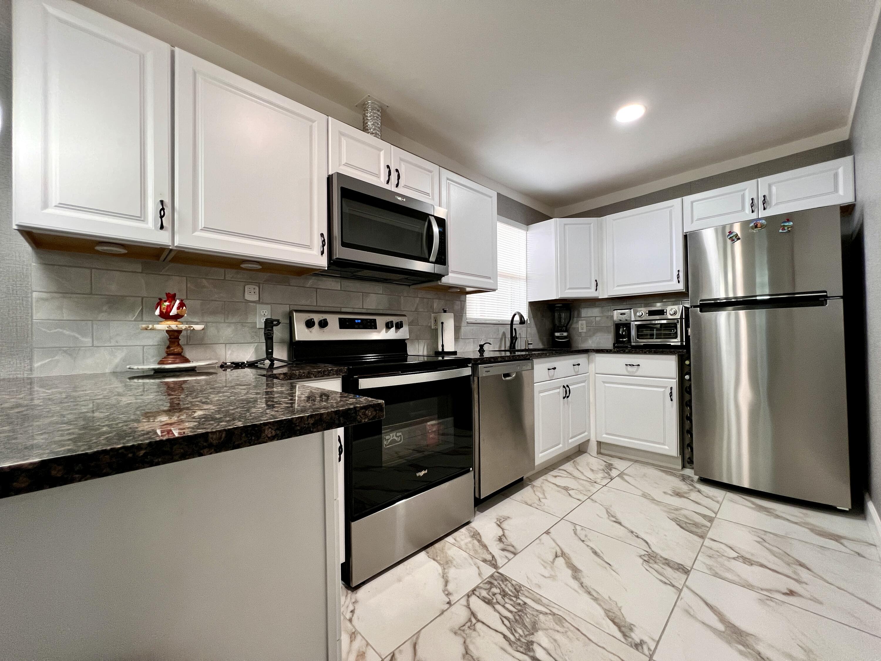 a kitchen with granite countertop a refrigerator sink and white cabinets