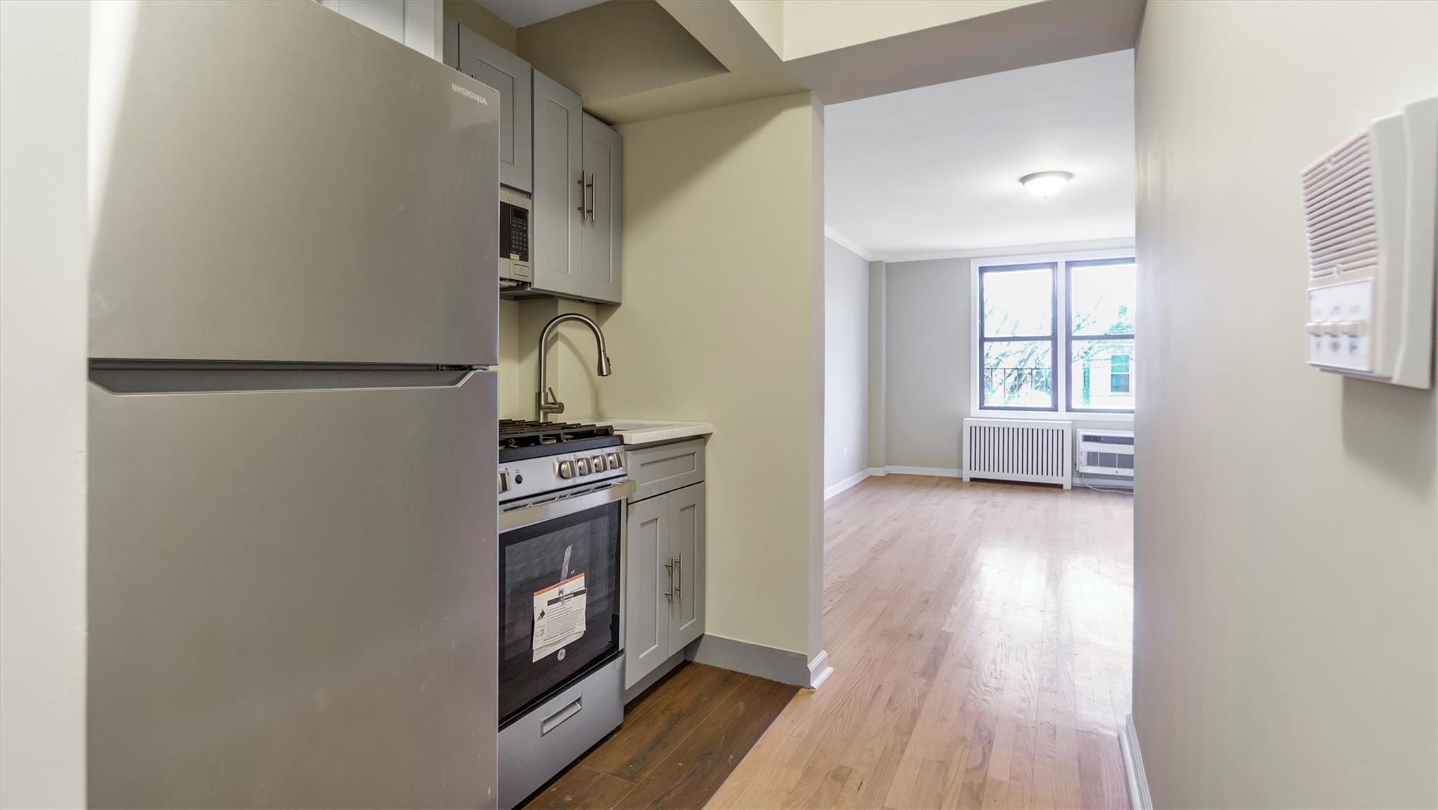 Kitchen with appliances with stainless steel finishes, crown molding, wood-type flooring, radiator heating unit, and gray cabinets