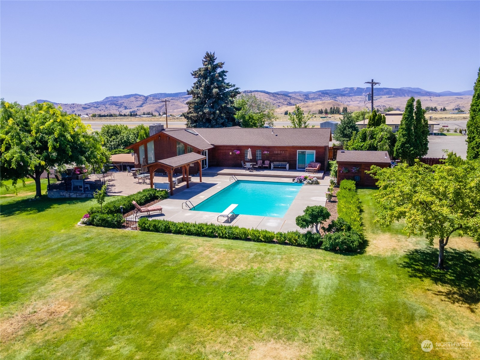 an aerial view of a house with swimming pool a playground lake and mountain view in back