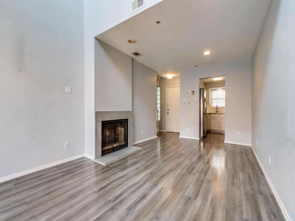 a view of an empty room with wooden floor fireplace and a window