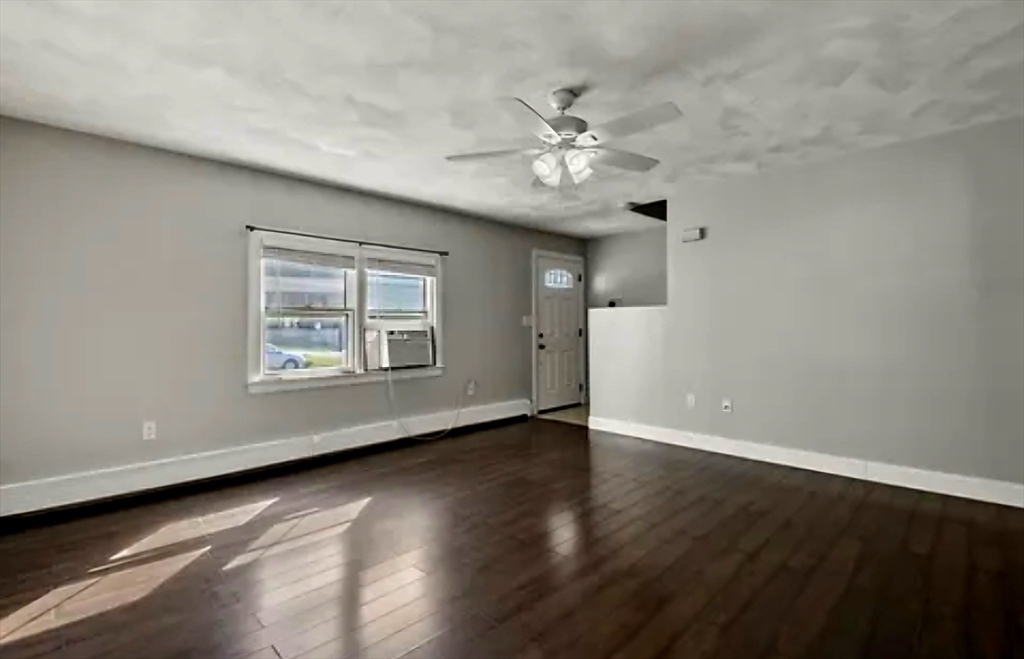 an empty room with wooden floor chandelier fan and windows