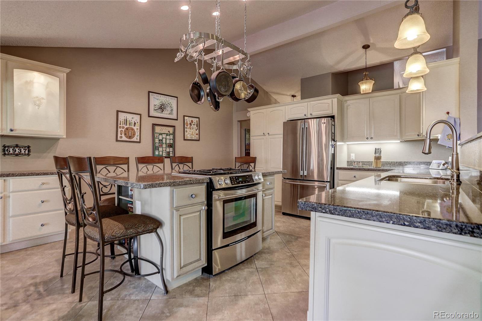 a kitchen with stainless steel appliances granite countertop a sink a stove a refrigerator cabinets and chairs