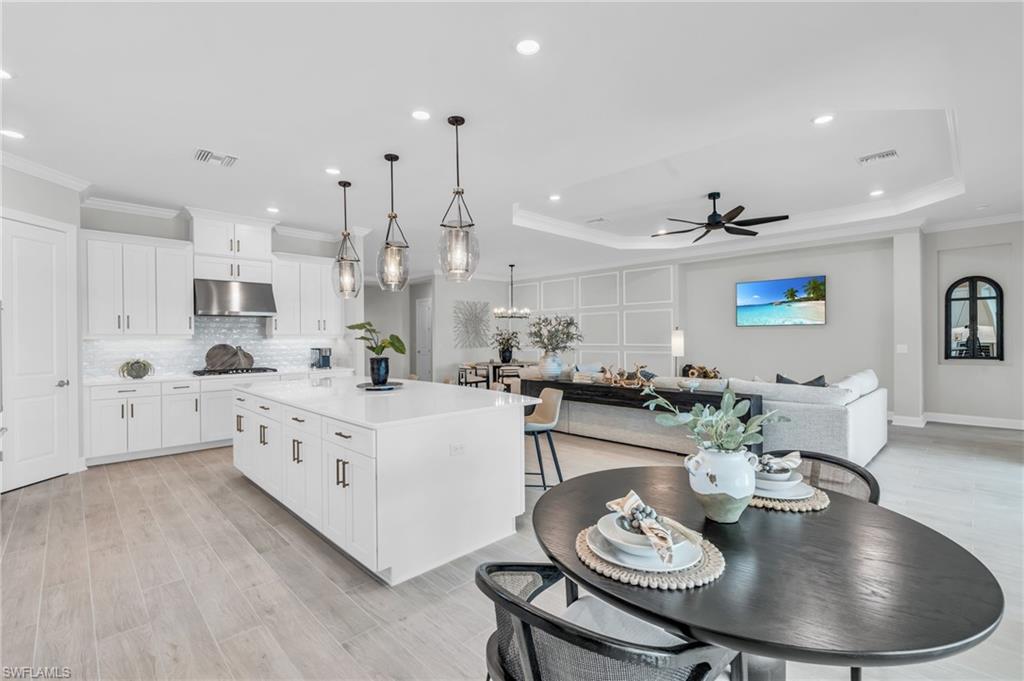 Kitchen featuring a tray ceiling, light hardwood / wood-style floors, a center island, white cabinetry, and ceiling fan