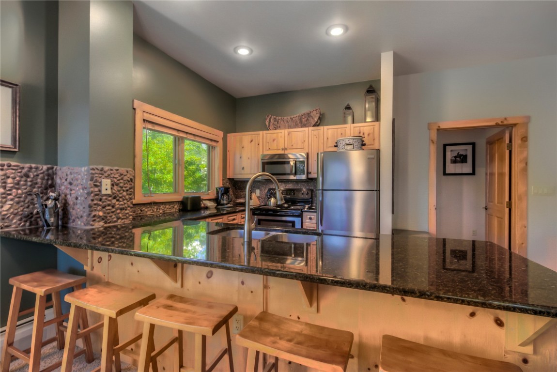 Kitchen with knotty pine cabinetry, granite kitchen island, tasteful backsplash, appliances with stainless steel finishes