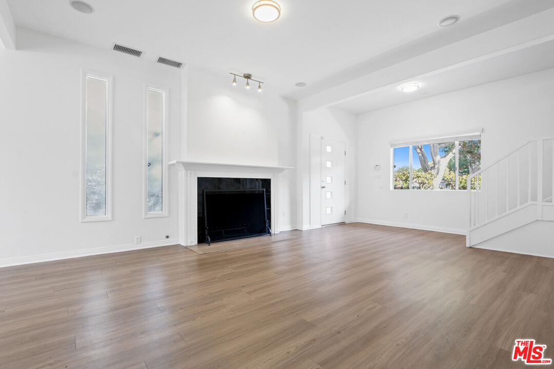 an empty room with wooden floor fireplace and windows