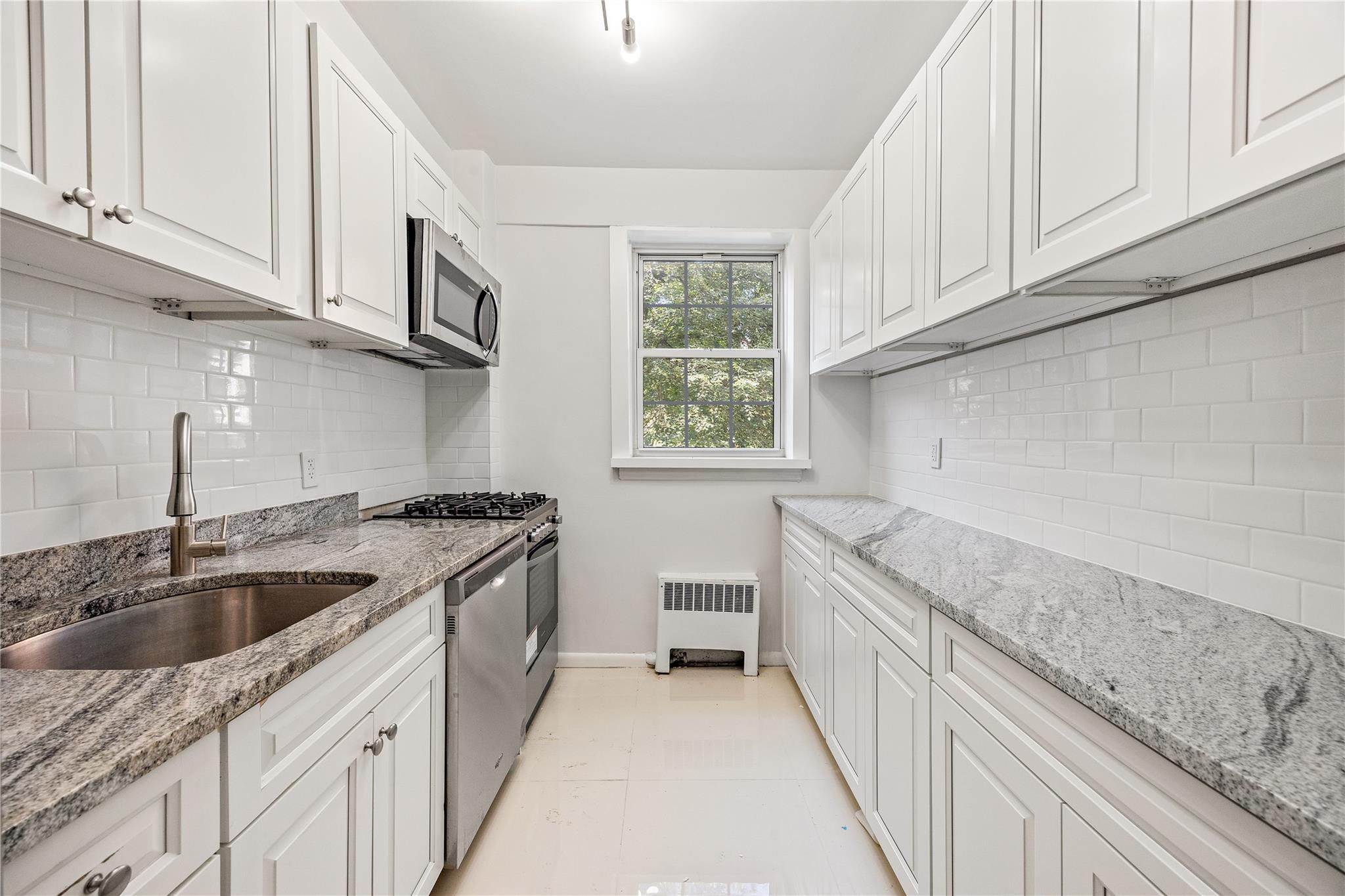 Kitchen with radiator heating unit, white cabinetry, sink, and appliances with stainless steel finishes