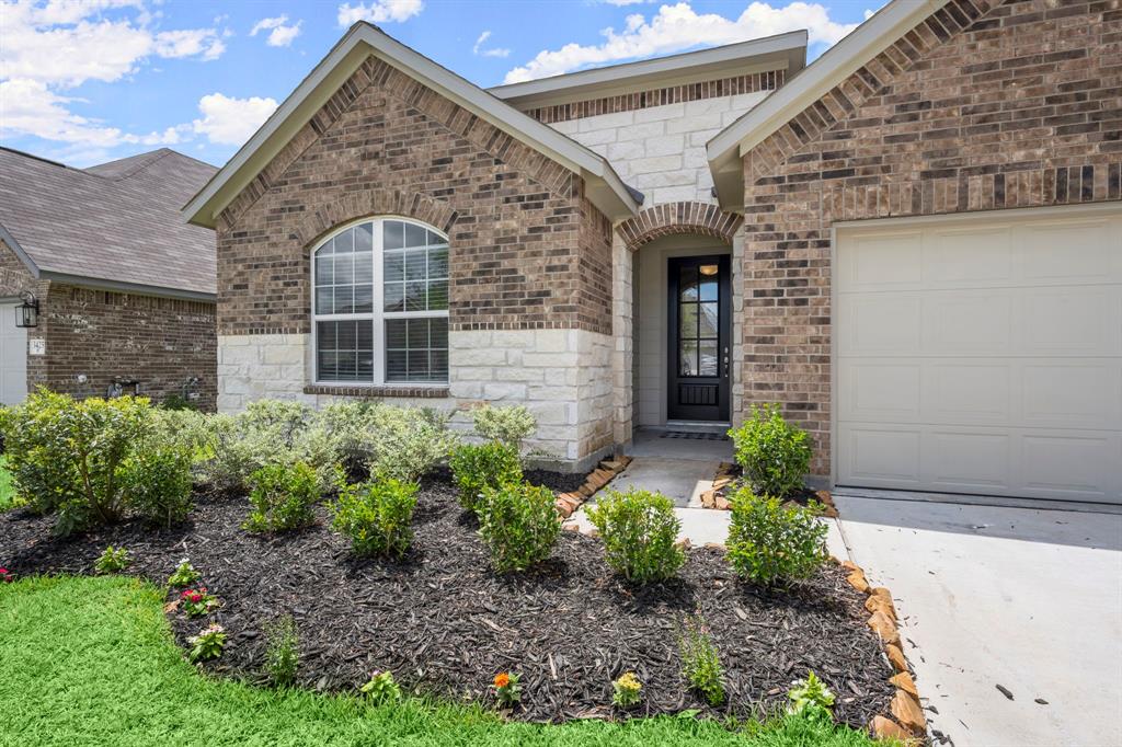 This is a single-story brick home featuring a large arched window, a well-maintained garden, and an attached two-car garage.